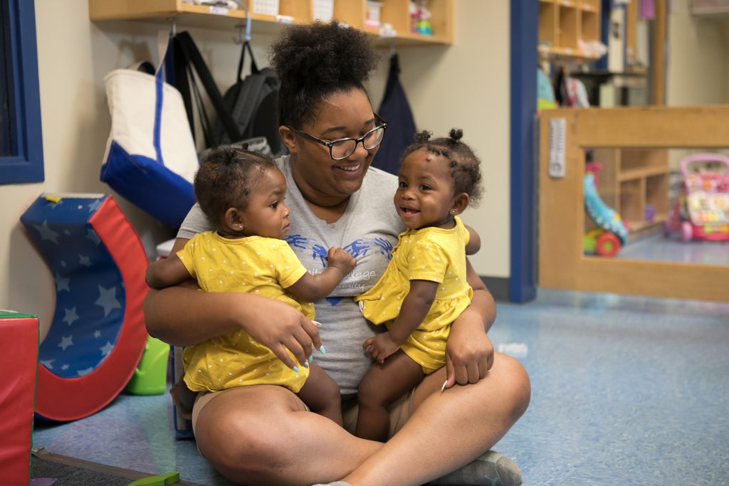 A teacher sits cross-legged holding twin baby girls