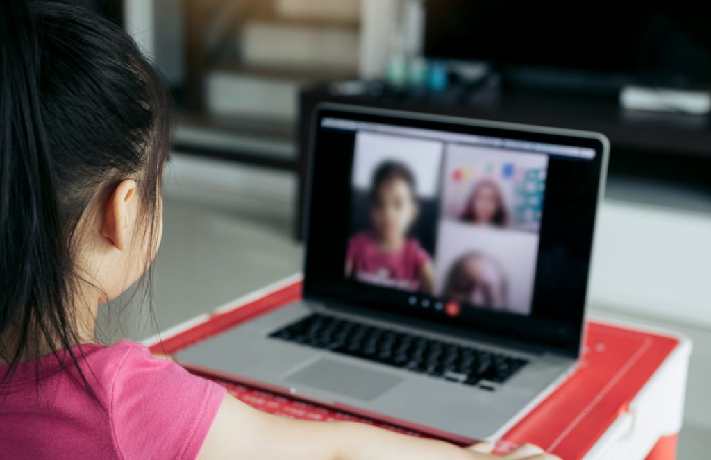 A girl sits in front of a laptop at home to take part in an online class.